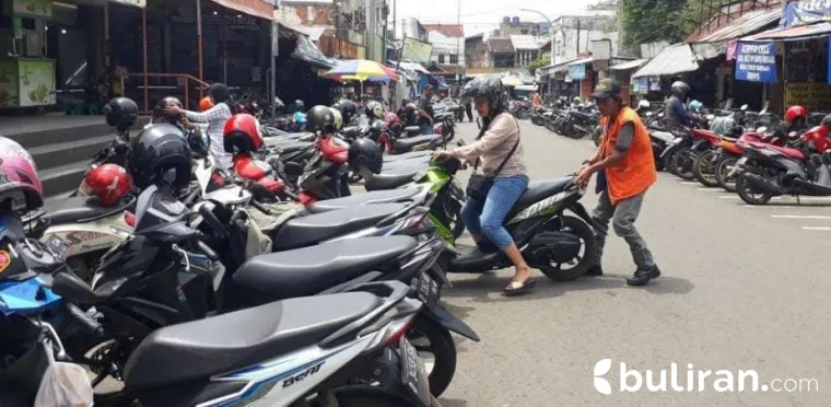 Tampilan seorang juru parkir yang sedang menata motor yang terparkir di atas trotoar.